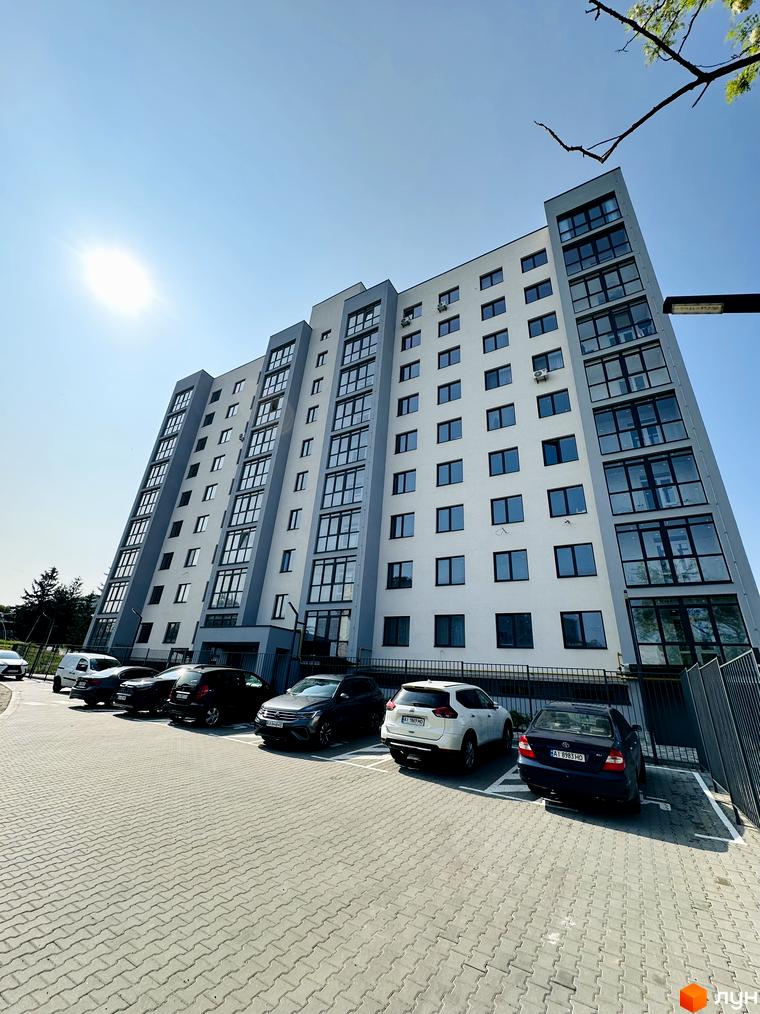 Багатоповерховий будинок Житлового комплексу Соборний світлого кольору з темними вікнами та скляними балконами. Перед будинком розташована вимощена парковка з автомобілями.