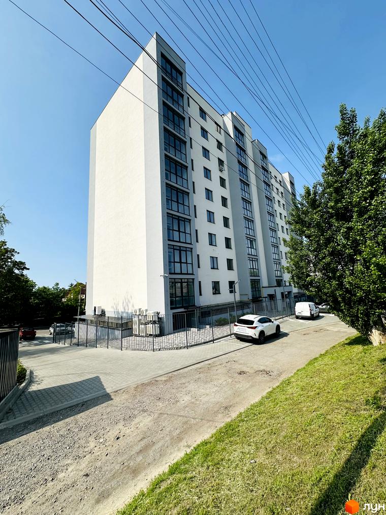 Житловий комплекс Соборний: багатоповерховий будинок з білими та сірими фасадами. На прибудинковій території парковка та зелені насадження.