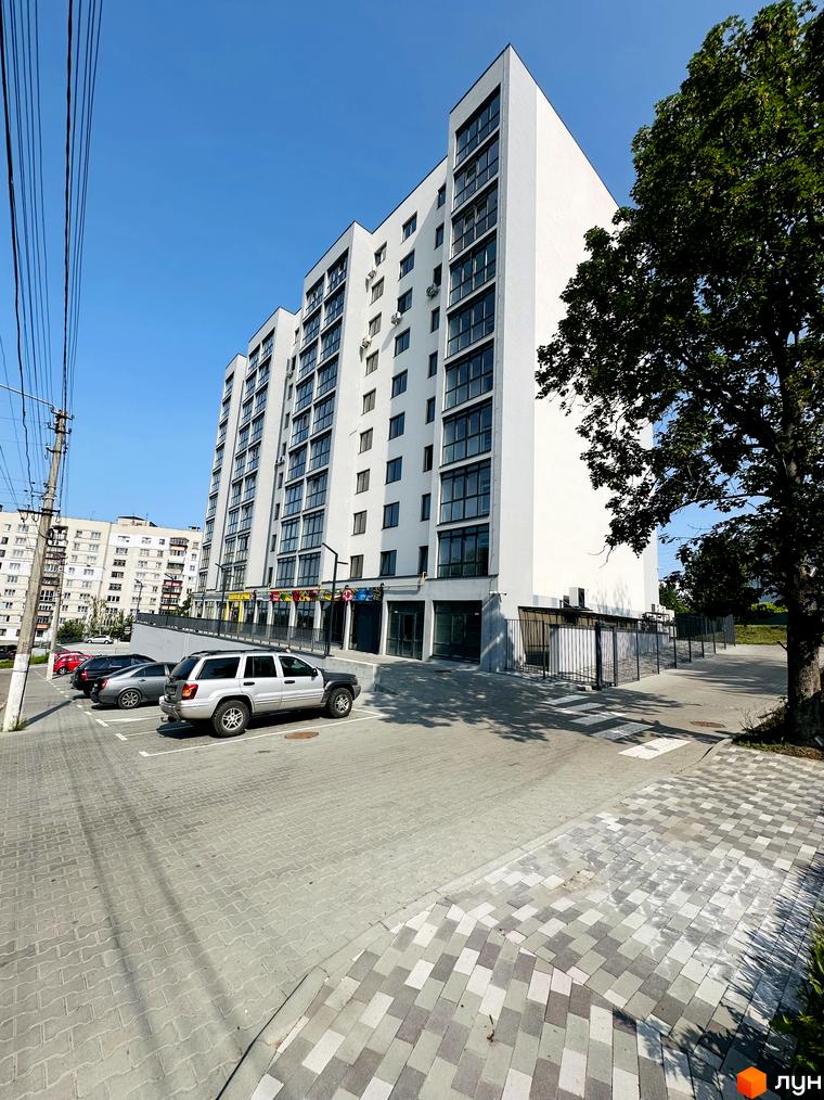 Багатоповерховий білий будинок Житлового комплексу Соборний з великими вікнами. Перед будинком розташований паркінг та зелені насадження.