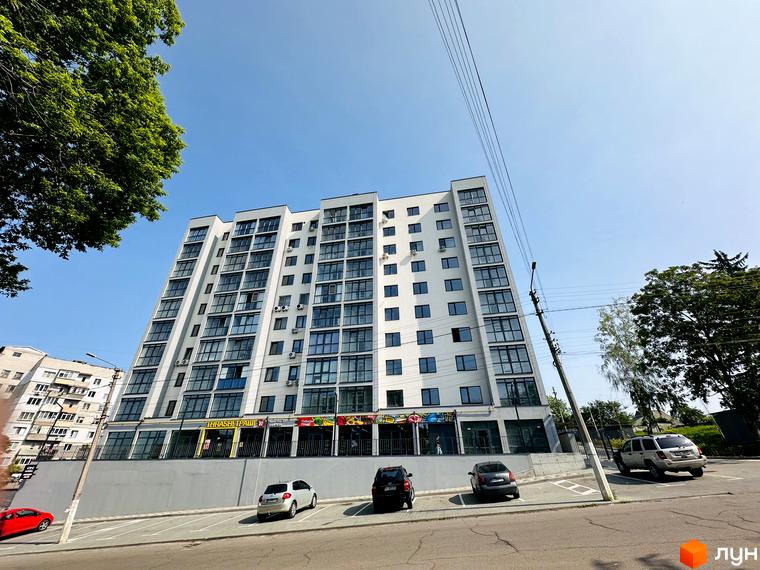 Житловий комплекс Соборний: білий багатоповерховий будинок з великими вікнами та комерційними приміщеннями на першому поверсі, оточений парковкою та деревами.