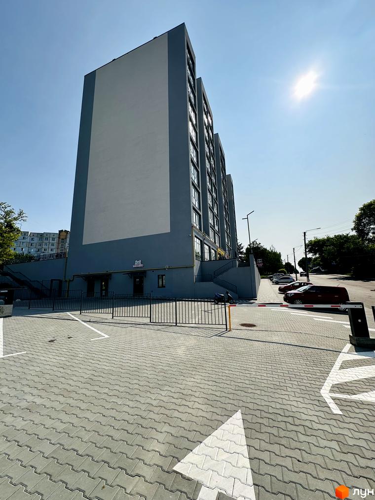 Житловий комплекс Соборний: багатоповерховий будинок сірого кольору з вікнами. Перед будинком вимощена територія з парковкою та шлагбаумом.