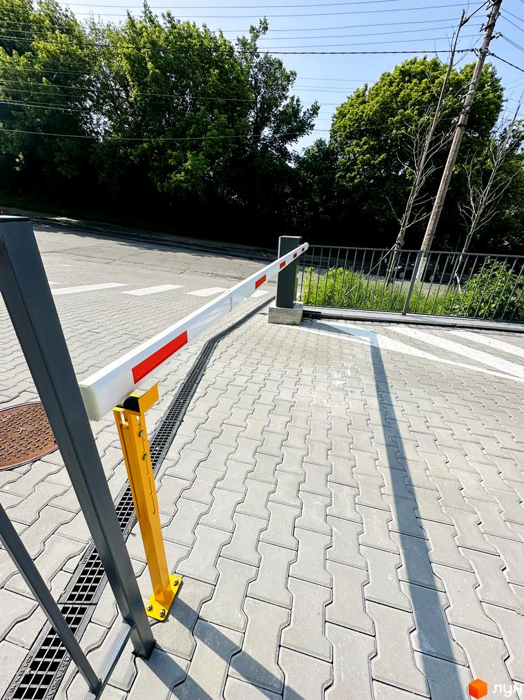 В'їзд до Житлового комплексу Соборний обладнаний опущеним шлагбаумом. Територія викладена сірою тротуарною плиткою.