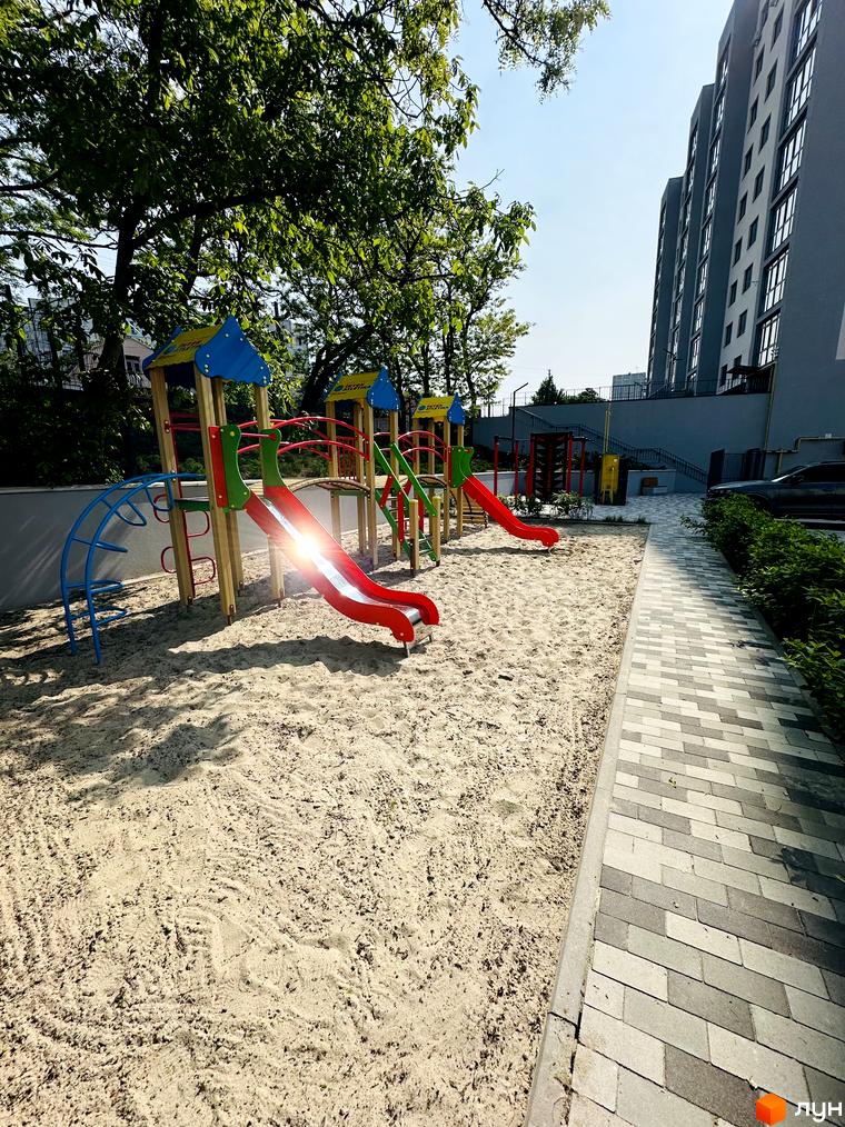 Будинок Житлового комплексу Соборний з сірим фасадом. Прибудинкова територія має дитячий майданчик з пісочницею та гірками.