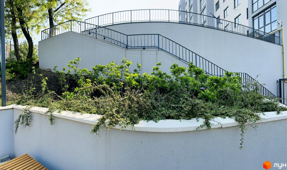 Багатоквартирний будинок Житлового комплексу Соборний зі світлим фасадом та зовнішніми сходами. Прибудинкова територія озеленена кущами та деревами.