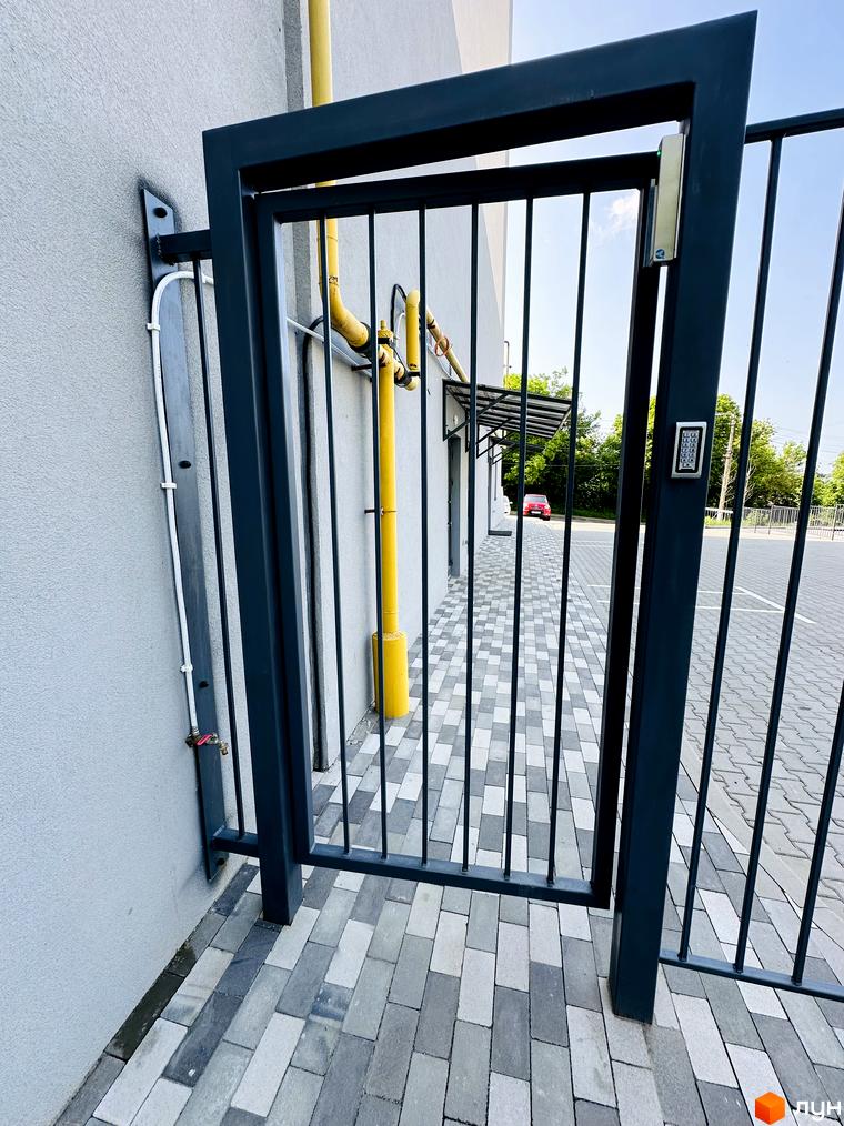 Вхід до Житлового комплексу Соборний з темною металевою брамою та кодовим замком. Перед будинком викладено сіру тротуарну плитку.