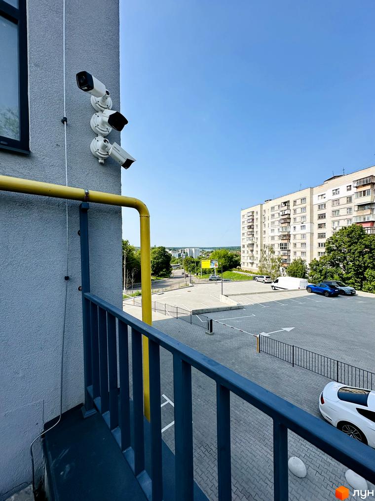 Вигляд на багатоповерховий будинок Житлового комплексу Соборний з камерами спостереження на фасаді. Прибудинкова територія з парковкою та зеленими насадженнями.