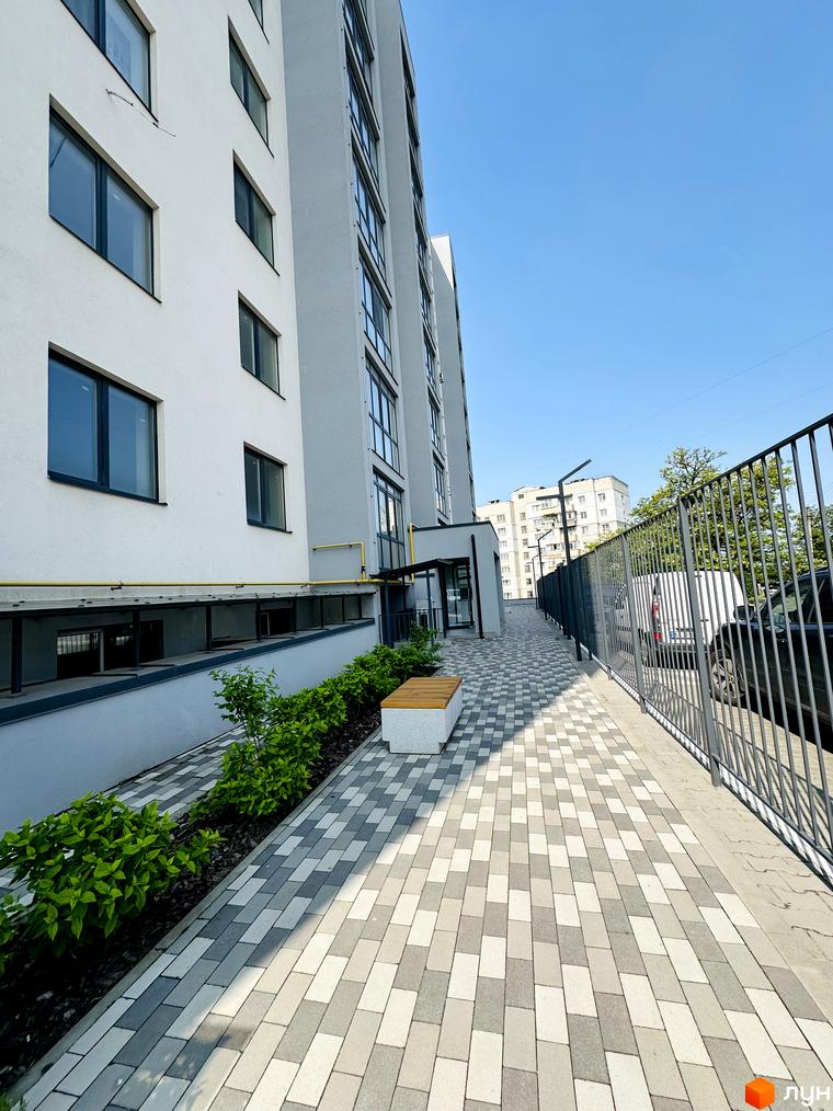 Багатоповерховий будинок Житлового комплексу Соборний з біло-сірим фасадом та темними вікнами. Перед будинком вимощена доріжка, зелені насадження та лавка.