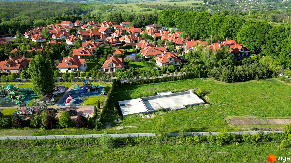 Фото Котеджне містечко Рославичі з виглядом на будинки з червоними дахами та зелену територію з дитячим майданчиком.