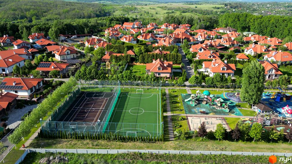 Вигляд Котеджного містечка Рославичі з червоними дахами. На території є спортивний майданчик, дитячий майданчик та зелені насадження.