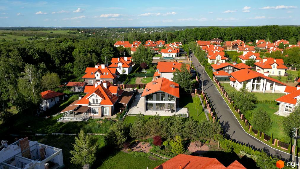 Зображення Котеджного містечка Рославичі з висоти пташиного польоту. Будинки з червоними дахами, зелена прибудинкова територія та асфальтована дорога.