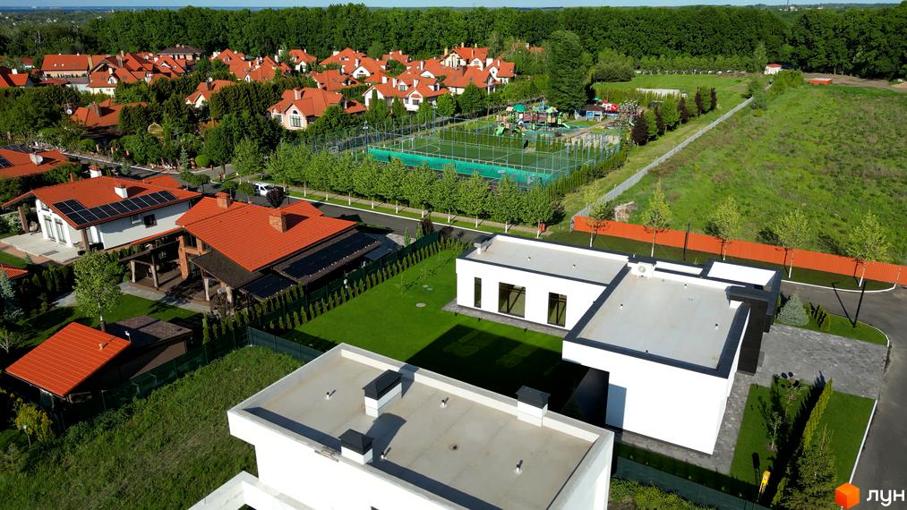 Вигляд Котеджного містечка Рославичі з сучасними будинками та зеленими газонами. На задньому плані видно дитячий майданчик та ліс.