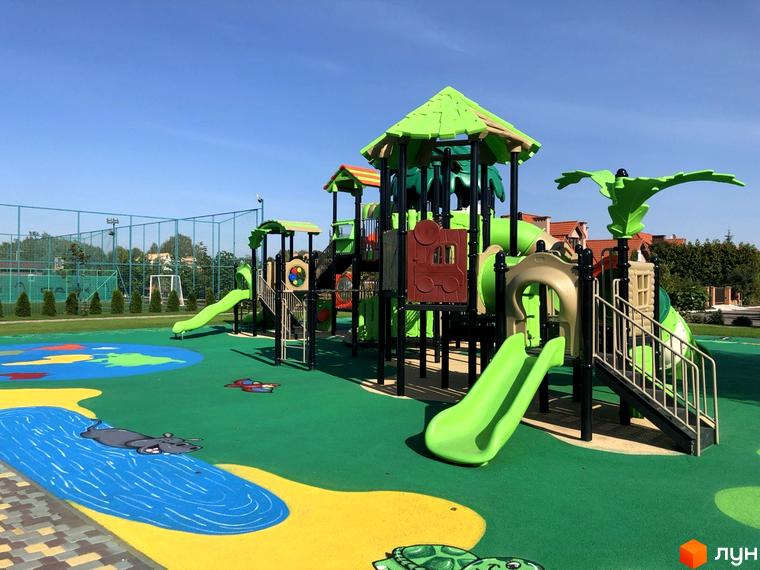 Дитячий майданчик з гірками та драбинками в Котеджному містечку Рославичі. Навколо зелений газон та дерева.