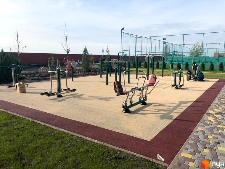 Зображення спортивного майданчика в Котеджному містечку Рославичі. На майданчику розташовані тренажери та турніки для занять спортом на свіжому повітрі.