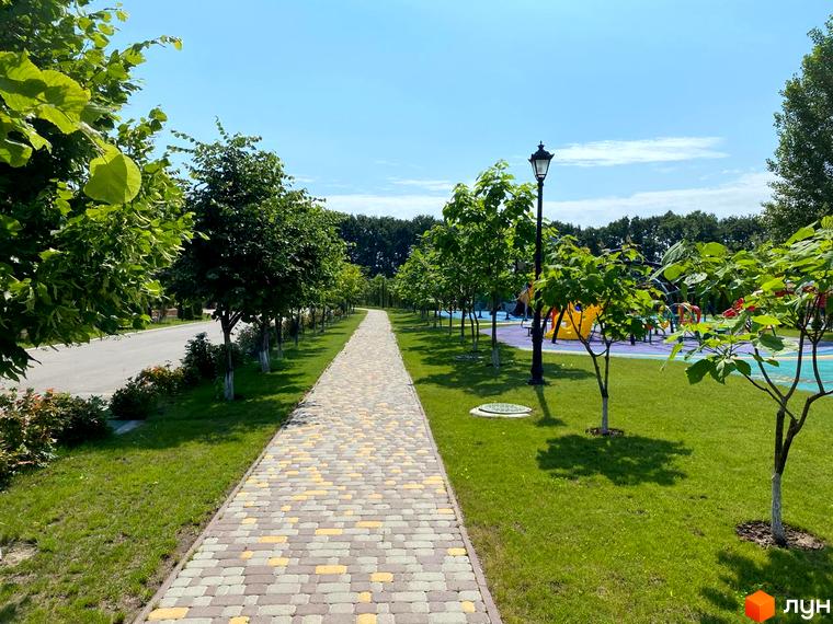 Вигляд пішохідної доріжки в Котеджному містечку Рославичі. Навколо зелені насадження та дитячий майданчик.