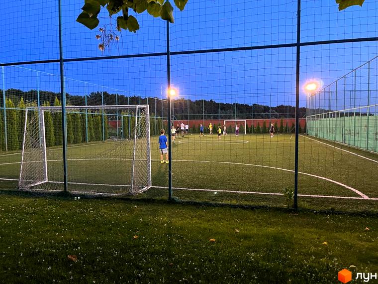 Зображення футбольного поля в Котеджному містечку Рославичі. На полі грають люди, видно ворота та освітлення.