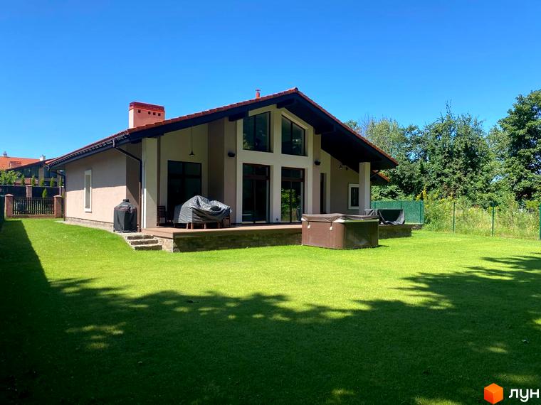 Вигляд будинку в Котеджному містечку Рославичі з великою галявиною перед ним. На задньому плані дерева та сусідні будівлі.