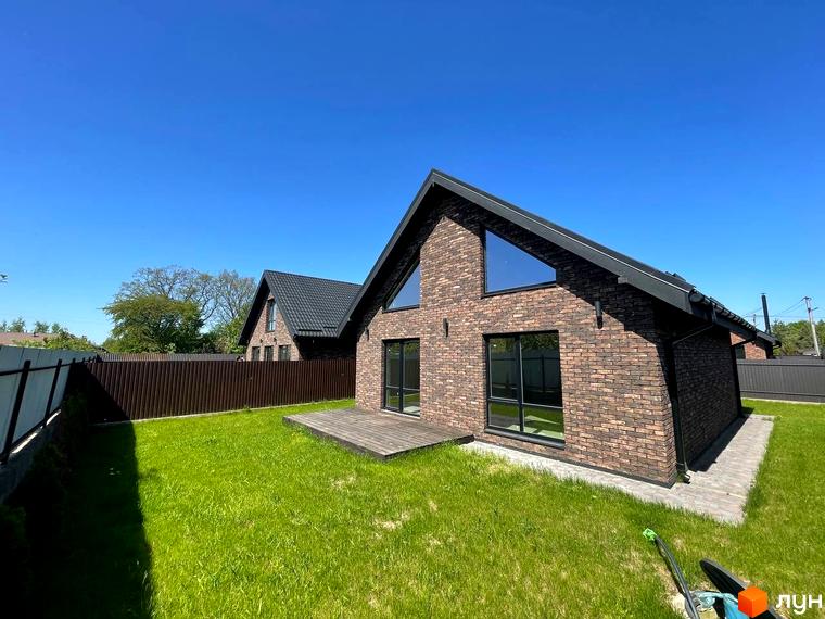 Котеджне містечко Одноповерховий Київ-Осокорки. Будинок з цегляним фасадом та великими вікнами, зелена галявина та дерев'яна тераса.