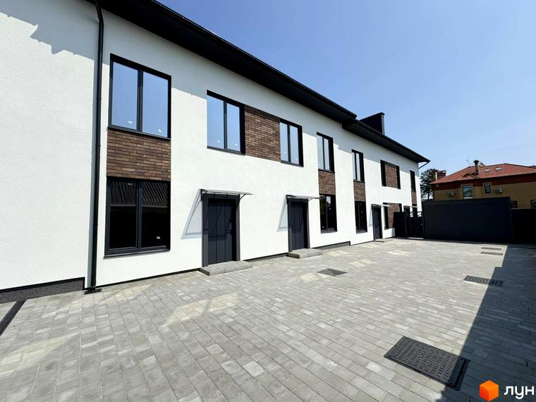 Зовнішній вигляд таунхаусів „В13“ з білими стінами, чорними вікнами та дверима, а також бруківкою на прибудинковій території.