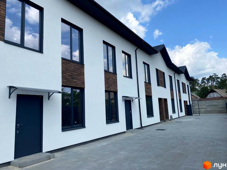 Таунхауси F12 - це двоповерхові будинки з білою штукатуркою та коричневими вставками, що виходять на вимощену сірою плиткою територію.