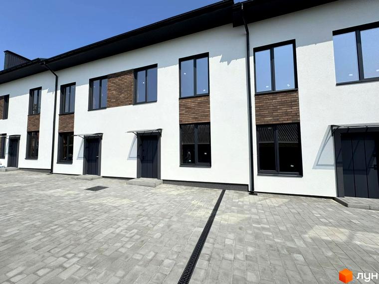 Зовнішній вигляд таунхаусів В13 з білими фасадами, чорними вікнами та цегляними вставками. Перед будинками облаштований сірий бруківковий двір.