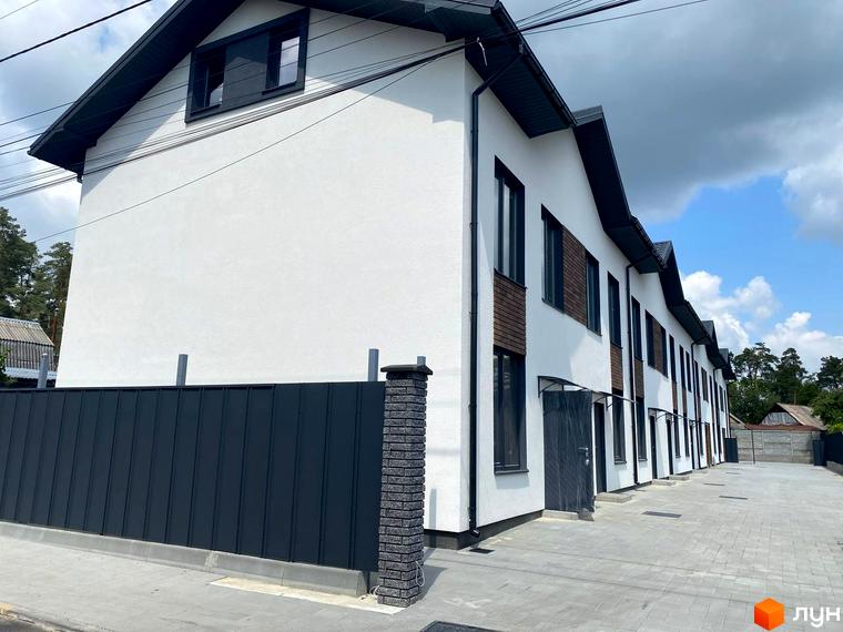 Таунхауси F12 – це сучасні двоповерхові будинки з білою штукатуркою та темними дахами, розташовані вздовж вимощеного бруківкою подвір'я з парканом.