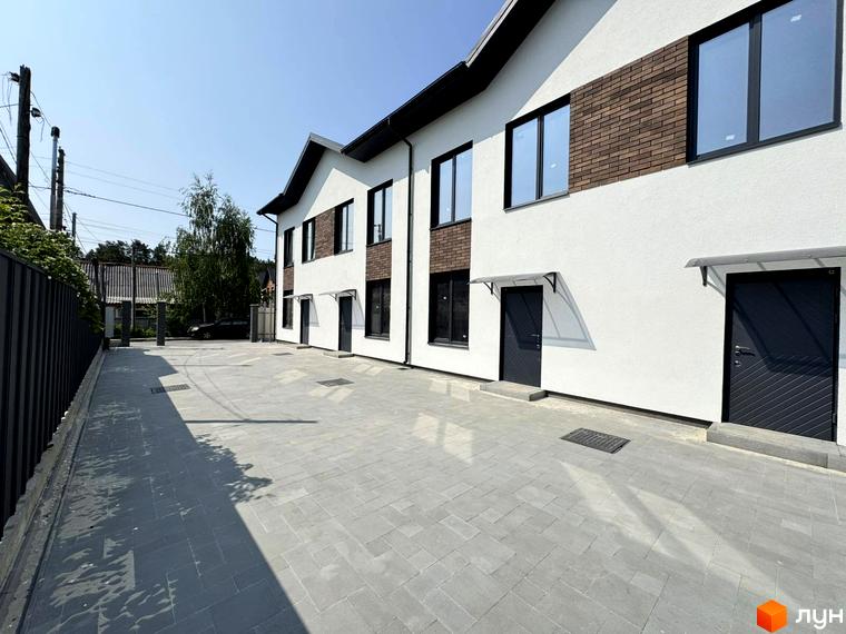 Таунхауси F12 з білими фасадами та цегляними вставками, з сірим вимощенням та парканом. Зовнішній вигляд будинку та прибудинкова територія.