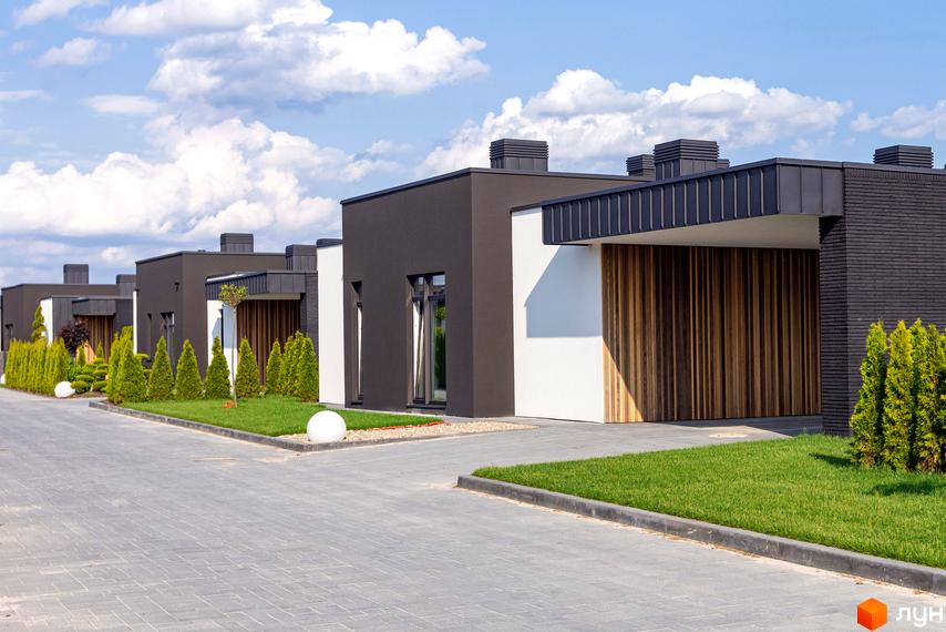 Котеджне містечко Terra Solis: сучасні будинки з дерев'яними фасадами та акуратними зеленими зонами. Асфальтована доріжка веде до будинків.