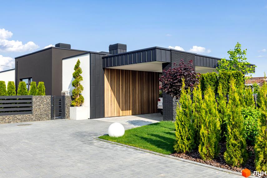 Фасад будинку в Містечко котеджів Terra Solis з дерев'яними воротами та доглянутою прибудинковою територією з газоном, рослинами та бруківкою.