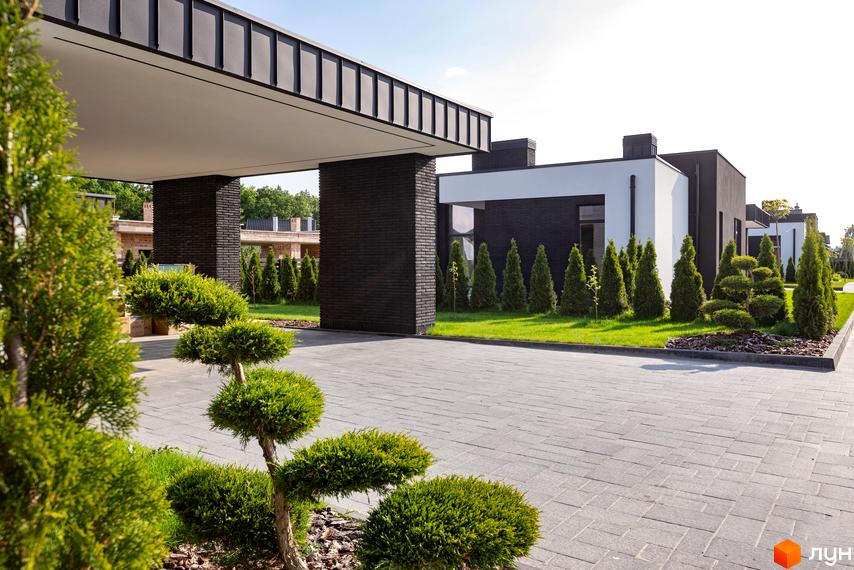 Фасад будинку в Котеджному містечку Terra Solis з темною цегляною обробкою та доглянутою прибудинковою територією з зеленими насадженнями.
