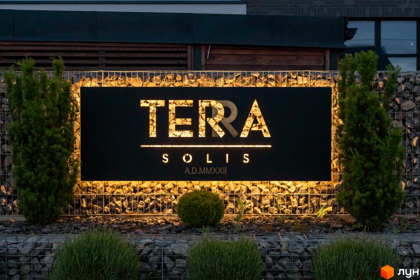Вивіска Містечка котеджів Terra Solis з підсвічуванням на тлі кам'яної огорожі та зелених насаджень.