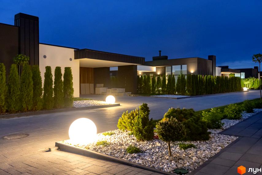 Зображення фасаду будинку в Котеджне містечко Terra Solis. На території розташовані декоративні кущі, газон та вуличні ліхтарі.