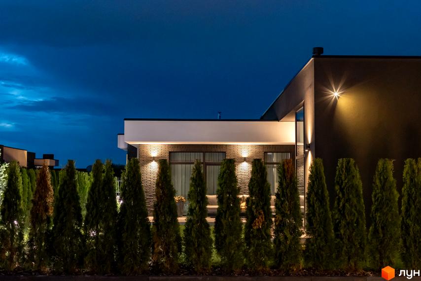Котеджне містечко КМ Terra Solis. Фасад будинку з цегляним оздобленням та підсвіткою, огороджений туями.