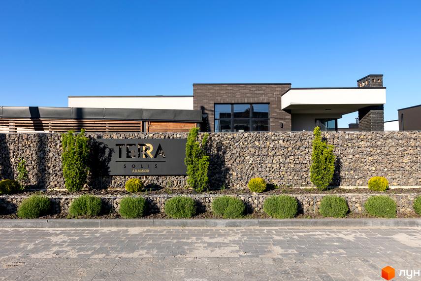 Зовнішній вигляд будинку КМ Terra Solis з фасадом з темної цегли та декоративного каменю. На передньому плані – доглянута прибудинкова територія з рослинами.