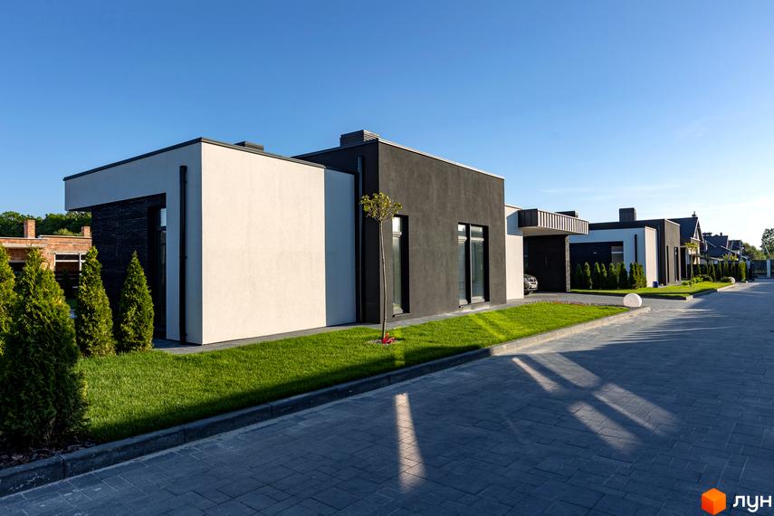 Будинки в Котеджному комплексі Terra Solis з білими та чорними фасадами, зеленою травою та бруківкою на території.