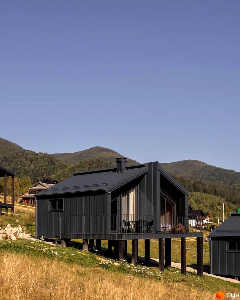 Котеджне містечко Barnhouse: сучасні будинки на палях у гірській місцевості з зеленими схилами та травою на передньому плані.