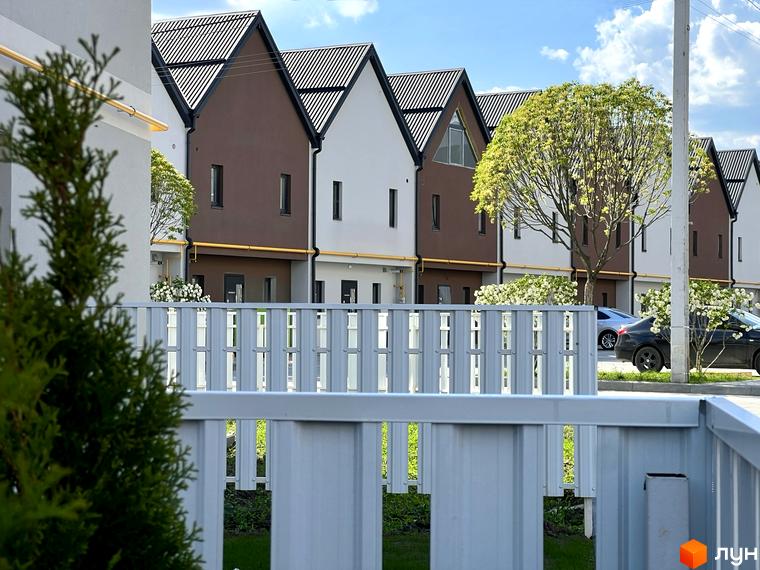 Будинки ЖК Sanville Park з коричневими та білими фасадами, розташовані поруч з зеленими насадженнями та білим парканом.