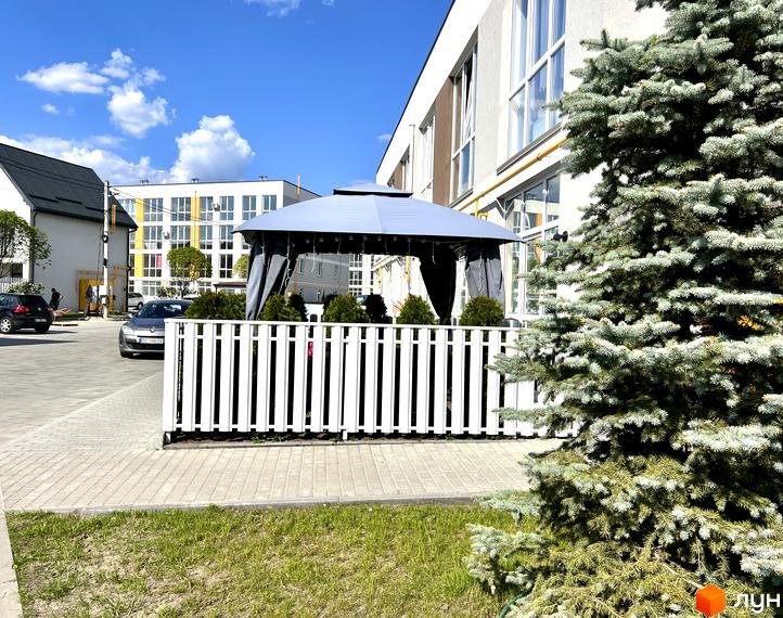 Житловий комплекс Sanville Park: білі будинки з великими вікнами, прибудинкова територія з газоном, огорожею та альтанкою.