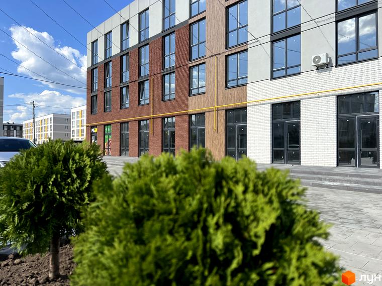 Зовнішній вигляд будівлі Житлового комплексу Sanville Park з фасадом з цегли та скла. На передньому плані зелені кущі, а на задньому – блакитне небо.