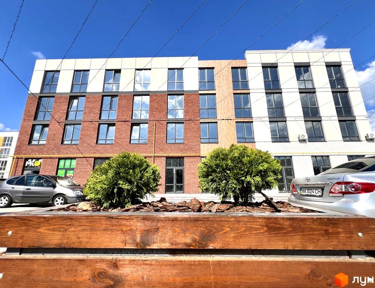 Зовнішній вигляд будинку Житловий комплекс Sanville Park з фасадом з цегли та великими вікнами. На передньому плані - декоративна клумба з рослинами.