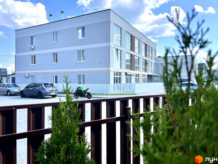 Житловий комплекс Sanville Park: триповерховий будинок світло-сірого кольору з білими вікнами. Перед будинком парковка з автомобілями та білий паркан.