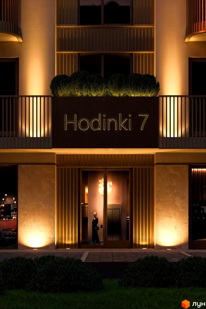Новобудова Hodinki 7 з підсвіченим фасадом та вхідною групою, оточена зеленню та газоном.