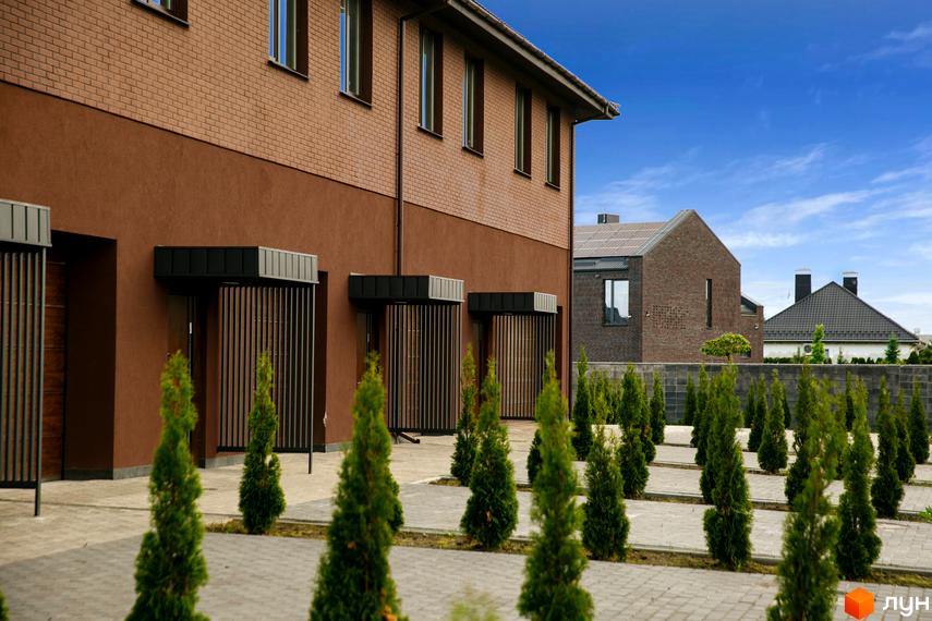 Фасад Комплексу клубного типу Обрій з коричневою цеглою та штукатуркою, вхідні групи з ламелями. Прибудинкова територія з вимощеною плиткою та зеленими насадженнями.