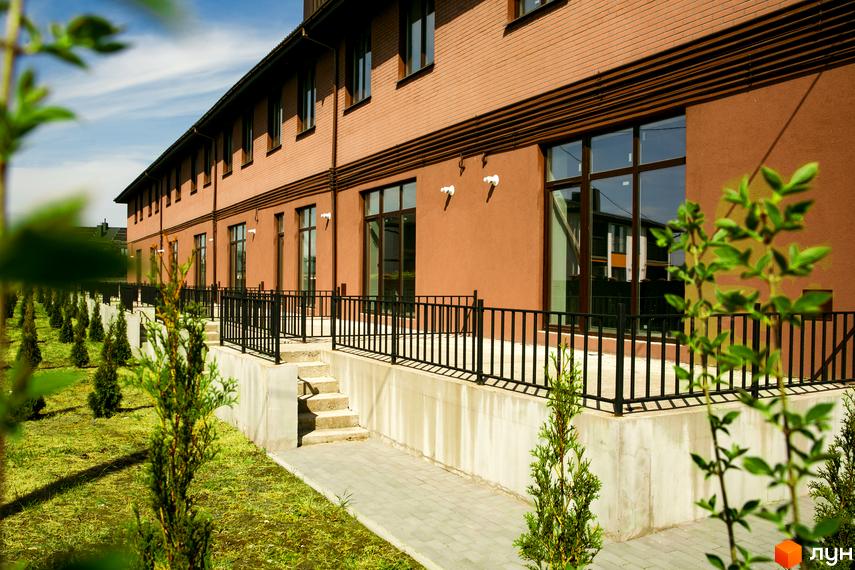 Будівля Житлового комплексу клубного типу Обрій з цегляним верхом та пофарбованим низом, великими вікнами. Прибудинкова територія має зелений газон з рядами молодих дерев.