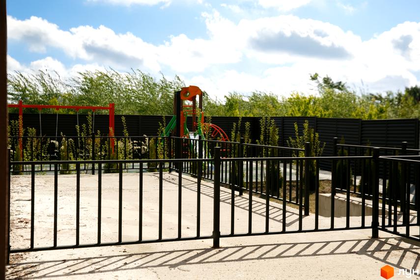 Фото дитячого майданчика в Житловому комплексі клубного типу Обрій. На задньому плані зелені насадження та огорожа.
