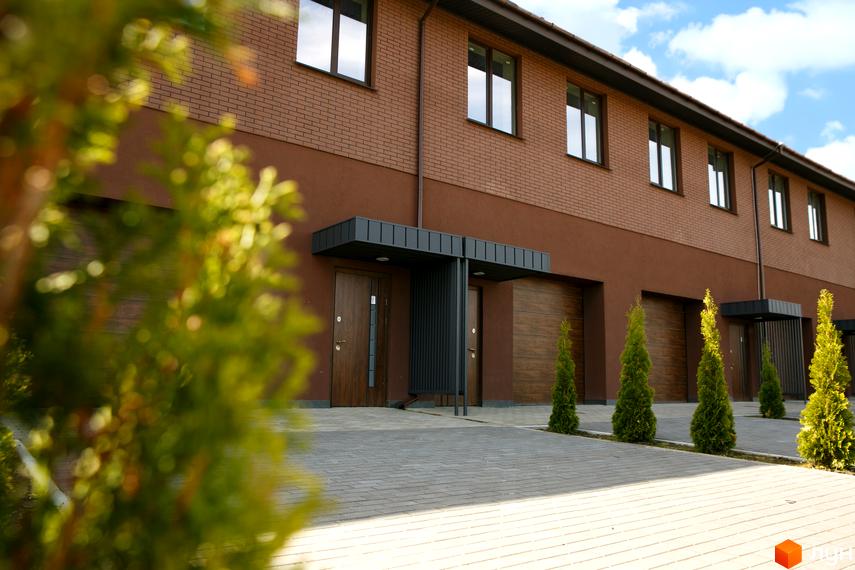 Житловий комплекс клубного типу Обрій: двоповерхові таунхауси з коричневою цегляною та штукатурною обробкою, дерев'яними воротами. Прибудинкова територія з бруківкою та хвойними деревами.