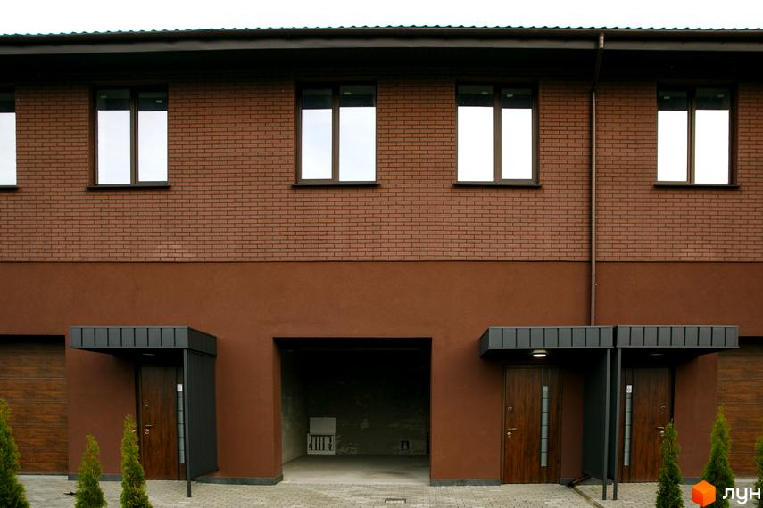 Фасад житлового комплексу клубного типу Обрій з коричневої цегли та штукатурки. Вхідні двері, гаражі, бруківка та зелені насадження біля будинку.