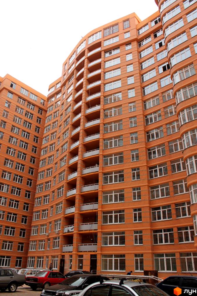 Житловий комплекс Люксембург з фасадом оранжевого кольору та балконами. Прибудинкова територія з автомобілями на парковці.