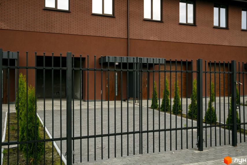 Зовнішній вигляд будинку в Житловому комплексі клубного типу Обрій. На передньому плані огорожа та зелені насадження.