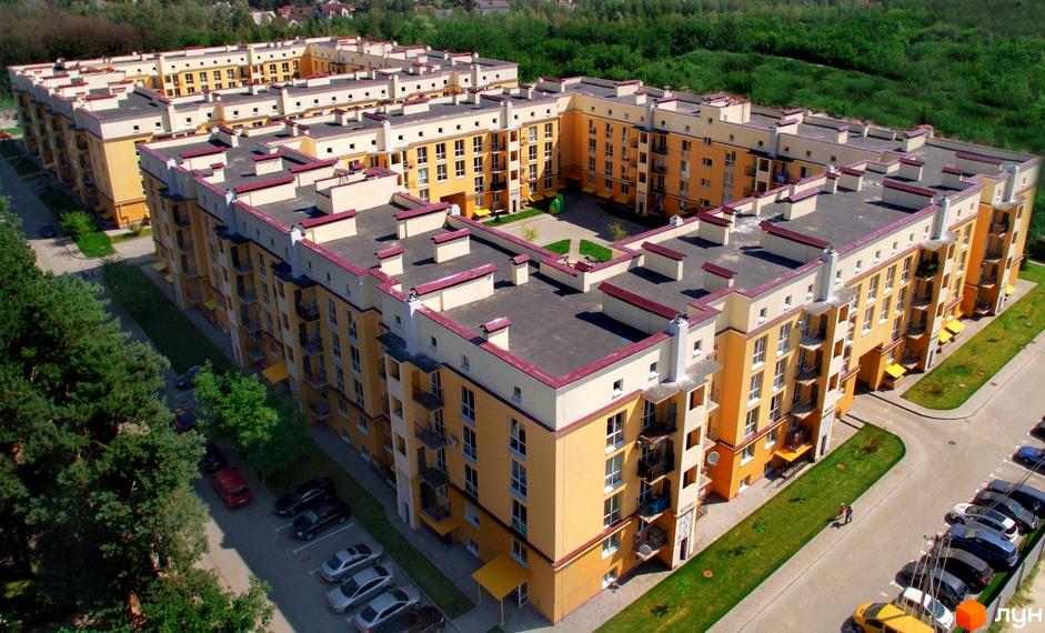 Житловий комплекс Сонцтаун - сучасна новобудова з жовтими фасадами та червоними дахами. Прибудинкова територія з зеленими газонами та парковкою.