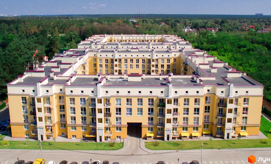 Зовнішній вигляд житлового комплексу Сонцтаун з жовтою фасадною частиною та сірими дахами. Навколо комплексу зелена зона та дорога з автомобілями.